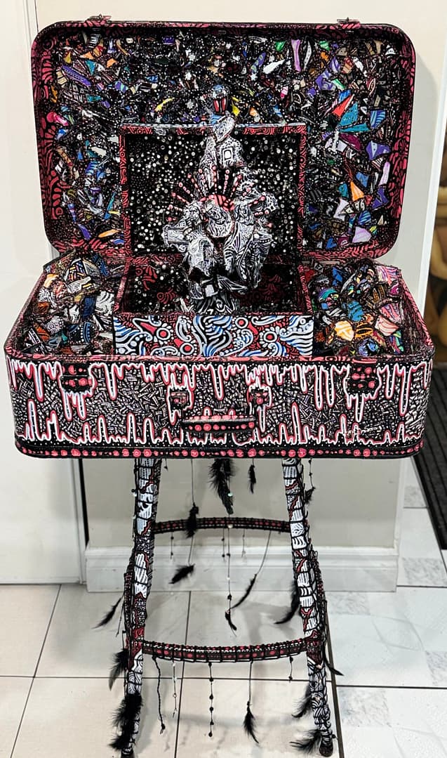 Video Mixed media sculptural figure by Cheyenne Sandoval featuring black feathers, beaded hood, and abstract blue and red patterning