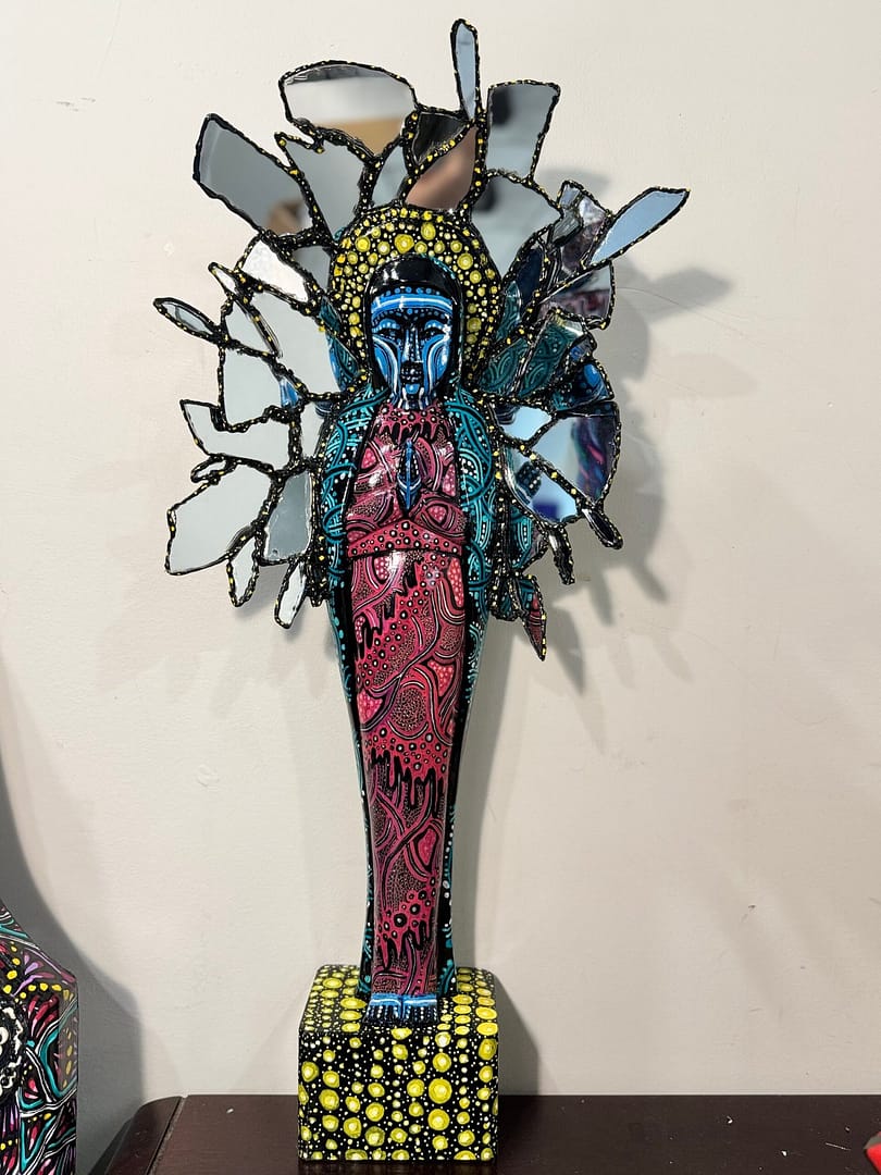 Studio Mixed media sculptural figure by Cheyenne Sandoval featuring black feathers, beaded hood, and abstract blue and red patterning