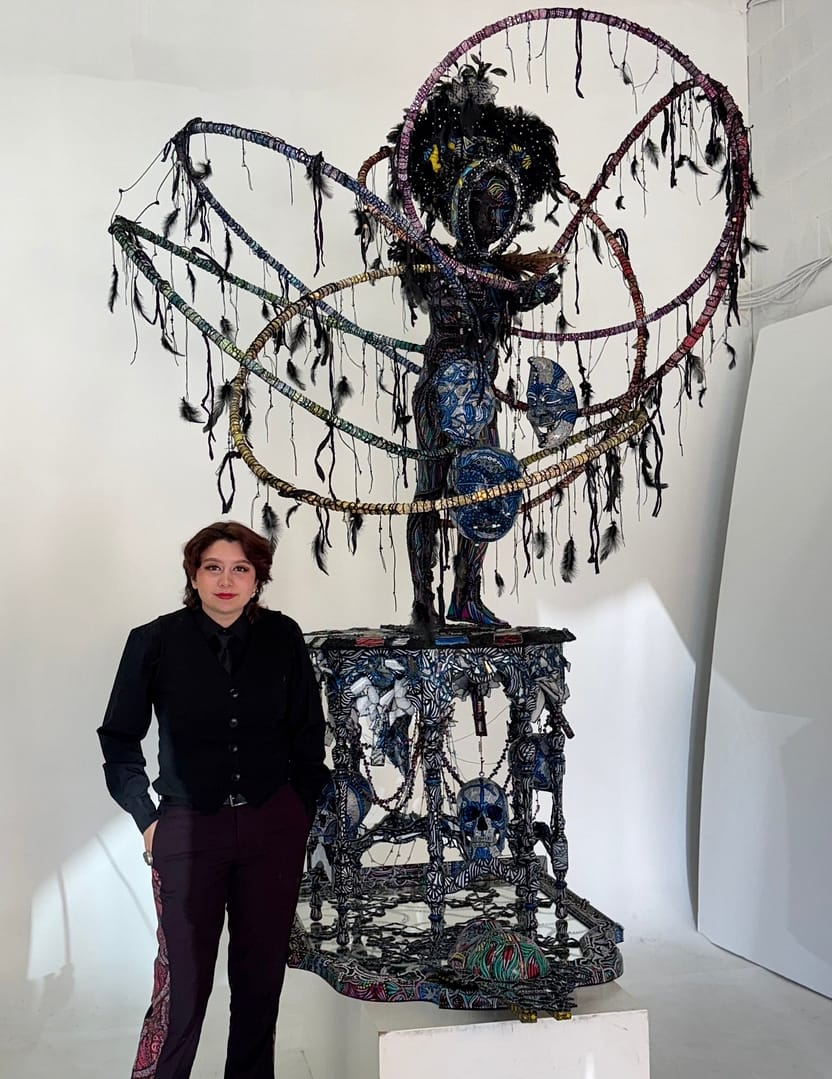 Studio Mixed media sculptural figure by Cheyenne Sandoval featuring black feathers, beaded hood, and abstract blue and red patterning