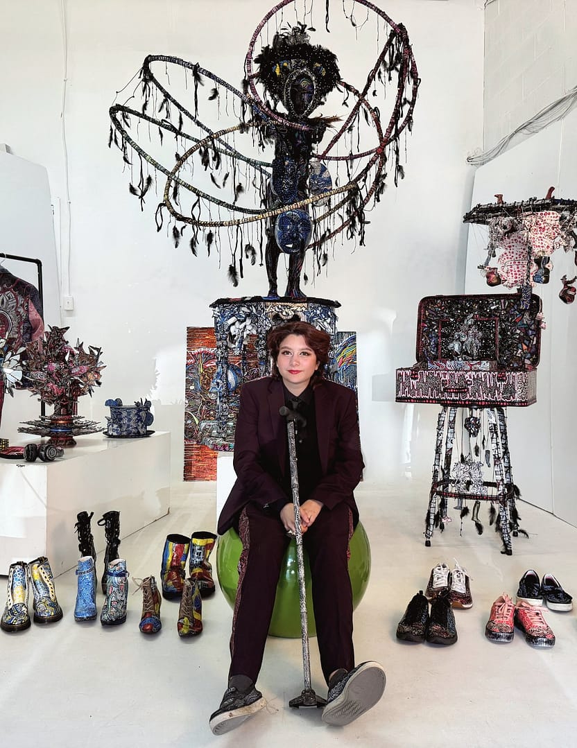 Studio Mixed media sculptural figure by Cheyenne Sandoval featuring black feathers, beaded hood, and abstract blue and red patterning