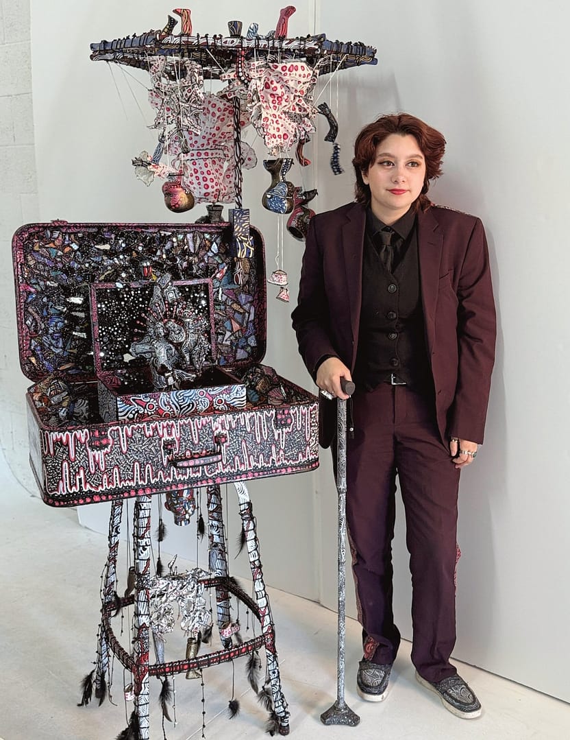 Studio Mixed media sculptural figure by Cheyenne Sandoval featuring black feathers, beaded hood, and abstract blue and red patterning